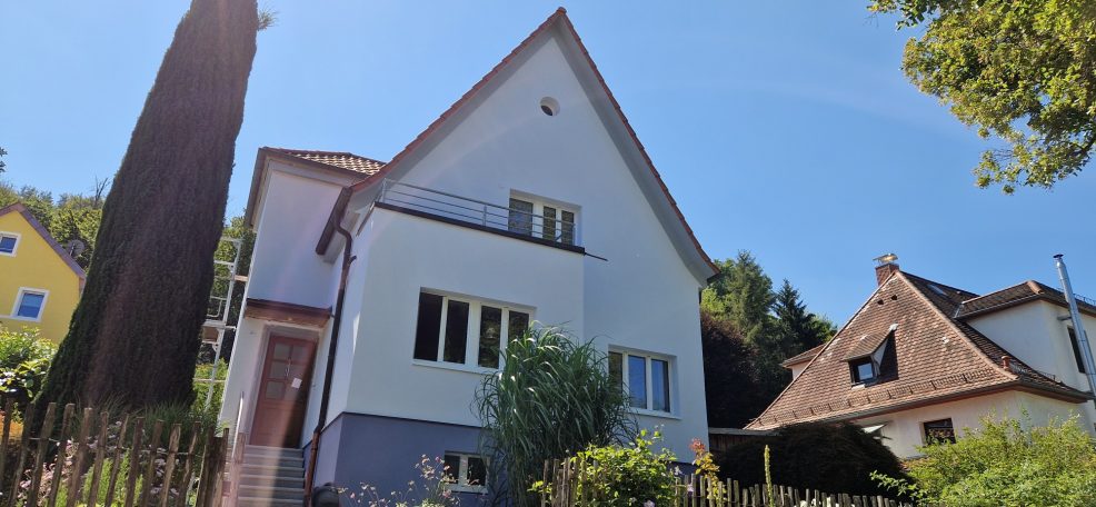 Fassadengestaltung Zwei-geschossiges Wohnhaus mit Giebel, umgeben von Pflanzen und Bäumen.