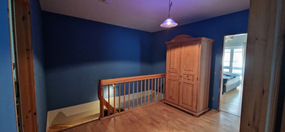 Malerarbeiten Ein blauer Raum mit Holztreppe und Kleiderschrank, Zugang zu einem weiteren Raum.